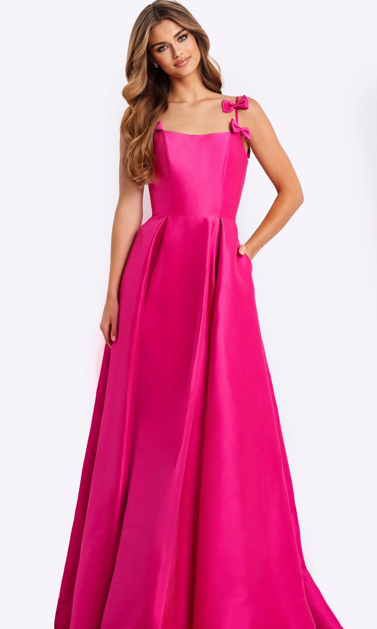A woman in the Jovani 46468 long prom dress in candy pink, featuring an A-line satin skirt and two bow accents on the shoulder straps, stands against a plain light background.